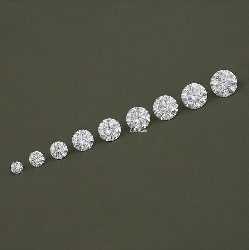 May include: A set of ten round, clear, faceted gemstones of varying sizes, arranged in a line from smallest to largest on a dark green background.