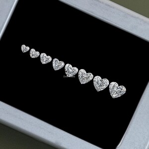May include: A row of heart-shaped diamonds of varying sizes, displayed in a black velvet box. The diamonds are clear and brilliant, with a high degree of clarity.