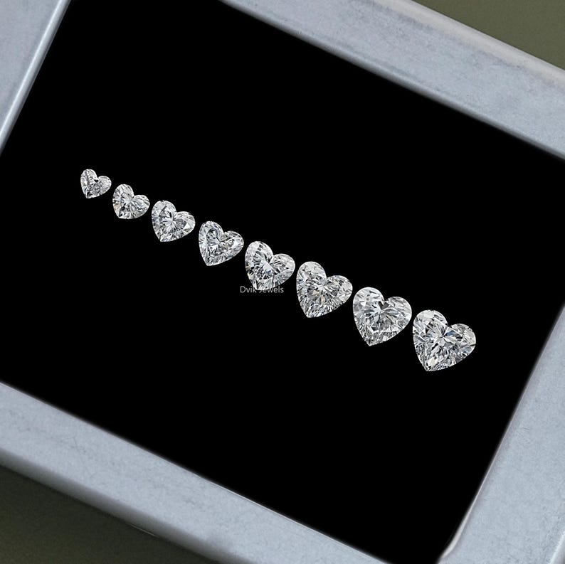 May include: A row of heart-shaped diamonds of varying sizes, displayed in a black velvet box. The diamonds are clear and brilliant, with a high degree of clarity.