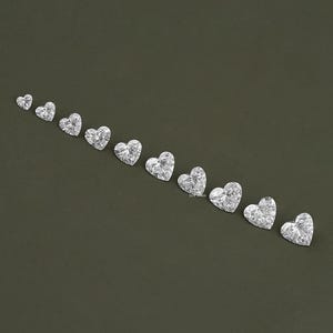 May include: A row of ten heart-shaped clear gemstones arranged in increasing size from left to right on a dark green background.