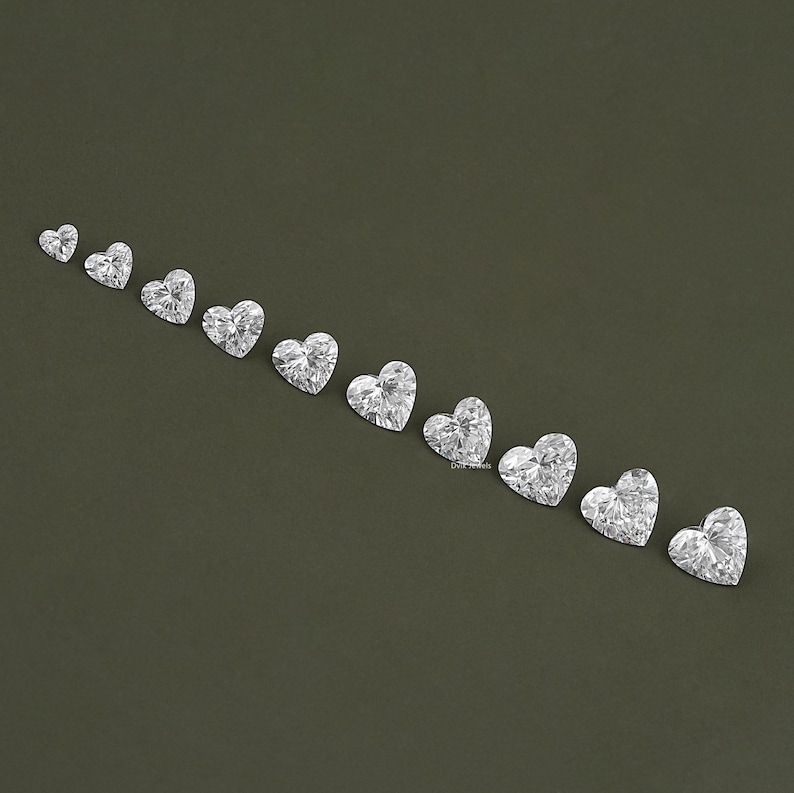May include: A row of ten heart-shaped clear gemstones arranged in increasing size from left to right on a dark green background.