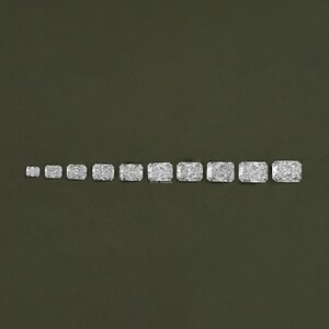May include: A row of ten clear, rectangular, faceted gemstones of varying sizes, arranged from smallest to largest on a green background.