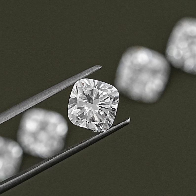 K&ouml;nnte beinhalten: Ein klarer, quadratischer Diamant, der mit einer Pinzette gehalten wird. Der Diamant ist von anderen &auml;hnlichen Edelsteinen umgeben.