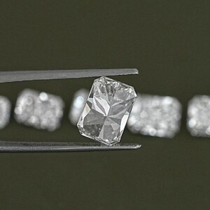 May include: A clear, rectangular, faceted gemstone held in tweezers. The gemstone is surrounded by other smaller, faceted gemstones.