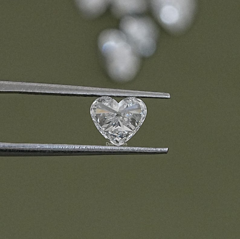 May include: A clear heart-shaped diamond held by tweezers against a green background.