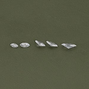 May include: Five clear marquise-shaped diamonds of varying sizes arranged in a row on a green background.