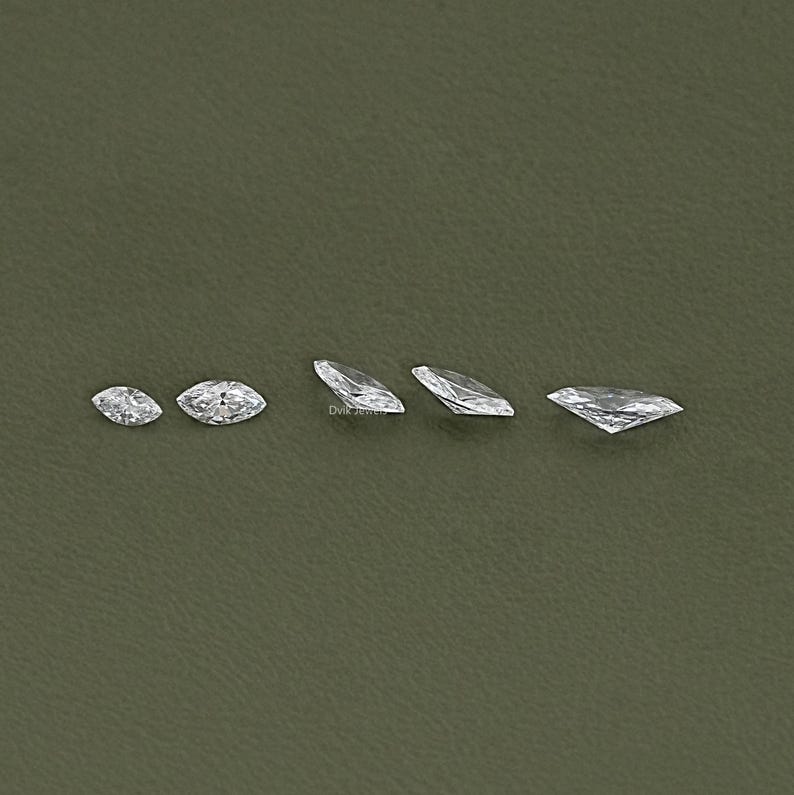 May include: Five clear marquise-shaped diamonds of varying sizes arranged in a row on a green background.