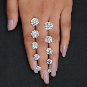 May include: A hand model displays a set of round, clear diamonds of varying sizes. The diamonds are arranged in a row on the fingers of the hand, with the largest diamond at the top and the smallest diamond at the bottom.