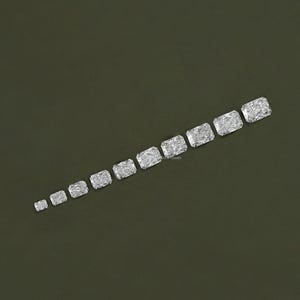 May include: A row of ten clear, rectangular, faceted gemstones of varying sizes, arranged in a diagonal line on a dark green background.