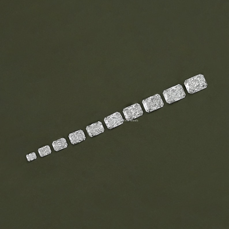 May include: A row of ten clear, rectangular, faceted gemstones of varying sizes, arranged in a diagonal line on a dark green background.