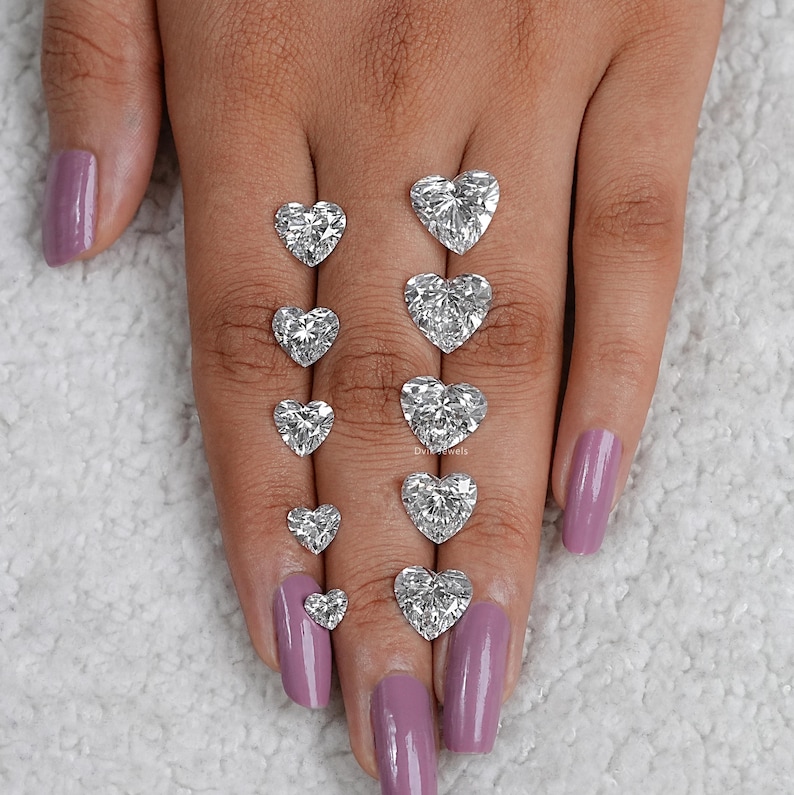 May include: A set of nine heart-shaped diamonds of varying sizes, displayed on a hand with pink nail polish.