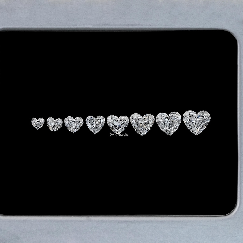 May include: A row of seven heart-shaped diamonds of varying sizes, arranged from smallest to largest. The diamonds are clear and sparkly, and they are set against a black background. The text "Divis Jewels" is visible below the diamonds.