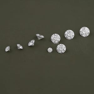 May include: A collection of ten clear round diamonds of varying sizes on a dark green background.