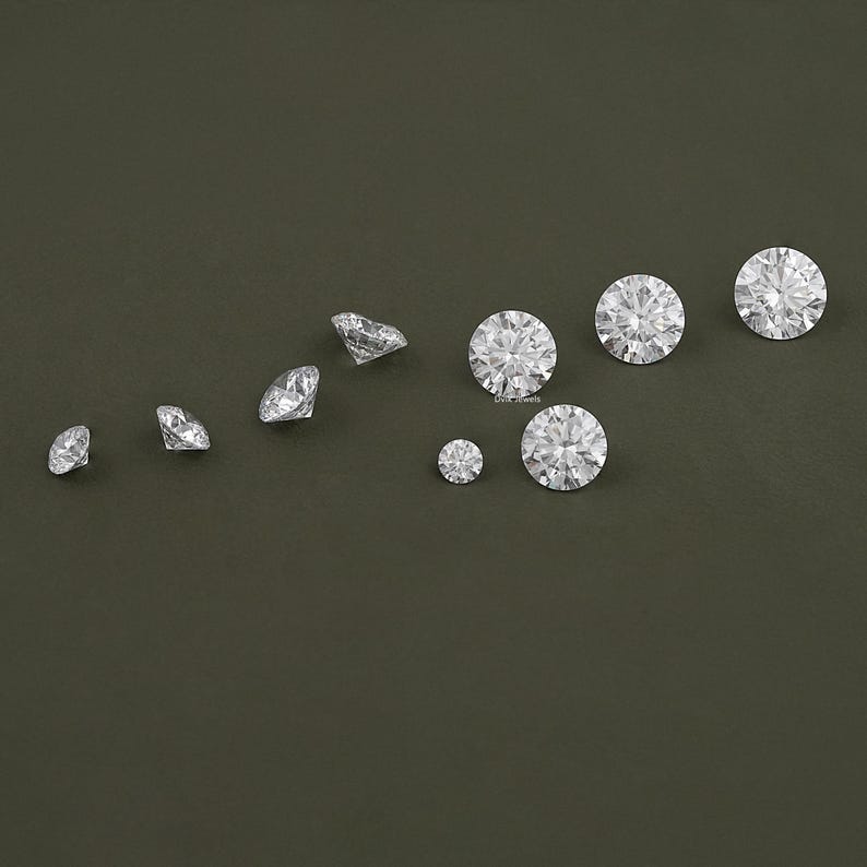 May include: A collection of ten clear round diamonds of varying sizes on a dark green background.