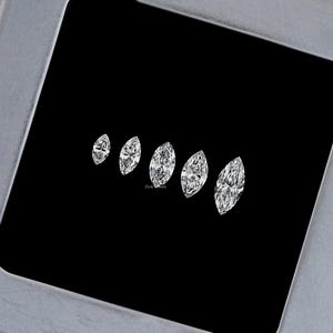 May include: Five marquise-shaped diamonds of varying sizes arranged in a row on a black background. The diamonds are clear and brilliant.