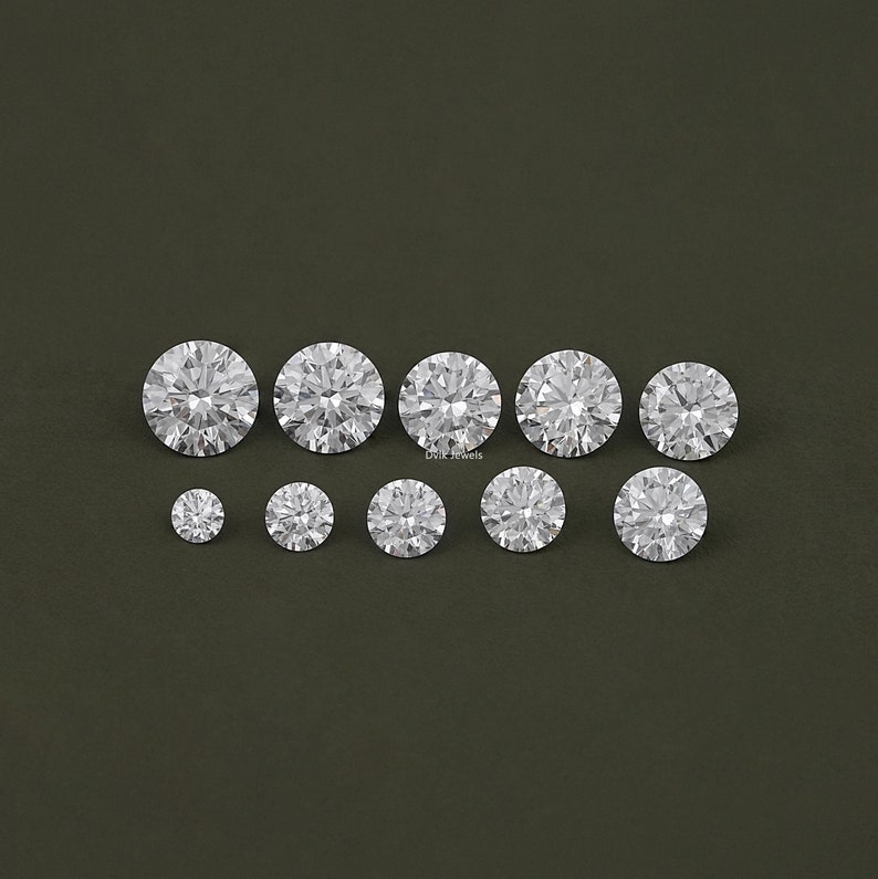 May include: A collection of ten round, clear, faceted gemstones. The gemstones are arranged in a row on a dark green background.