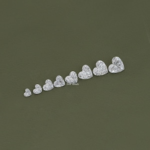 May include: A row of ten heart-shaped diamonds of varying sizes, arranged from smallest to largest, on a green background. The diamonds are clear and sparkly. The text "Divk Jewels" is visible at the bottom of the image.