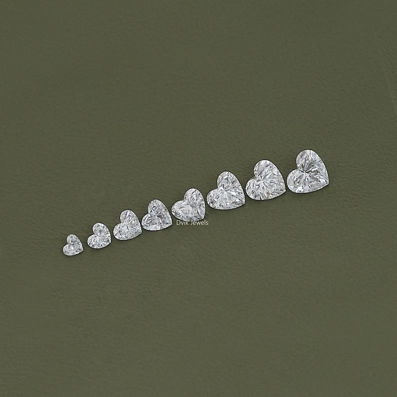 May include: A row of ten heart-shaped diamonds of varying sizes, arranged from smallest to largest, on a green background. The diamonds are clear and sparkly. The text "Divk Jewels" is visible at the bottom of the image.