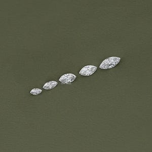 May include: A set of six marquise-shaped diamonds of varying sizes, arranged in a row on a green surface.
