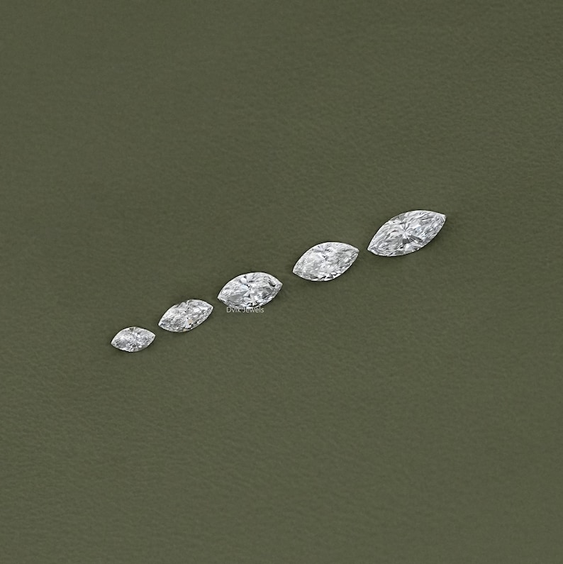 May include: A set of six marquise-shaped diamonds of varying sizes, arranged in a row on a green surface.
