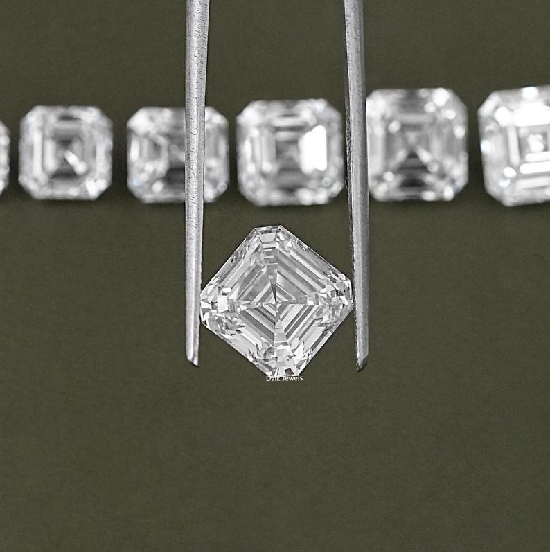 May include: A clear, square-shaped diamond gemstone held by tweezers. The diamond has a faceted cut and is surrounded by other similar diamonds.