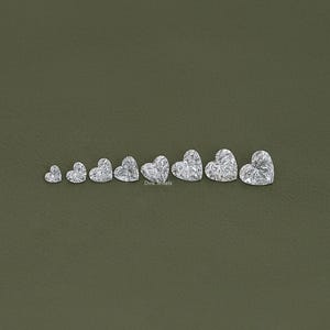 May include: A set of nine heart-shaped diamonds of varying sizes, arranged in a row from smallest to largest. The diamonds are clear and sparkly, and they are set against a green background.