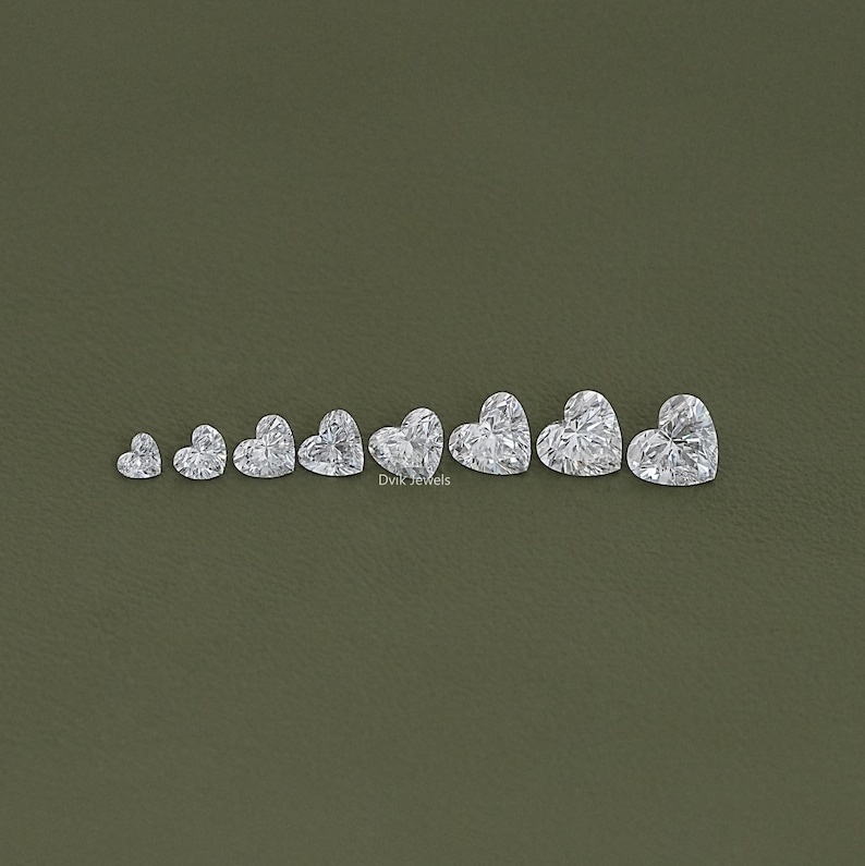 May include: A set of nine heart-shaped diamonds of varying sizes, arranged in a row from smallest to largest. The diamonds are clear and sparkly, and they are set against a green background.