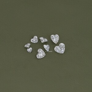 May include: A collection of clear heart-shaped gemstones on a green background.