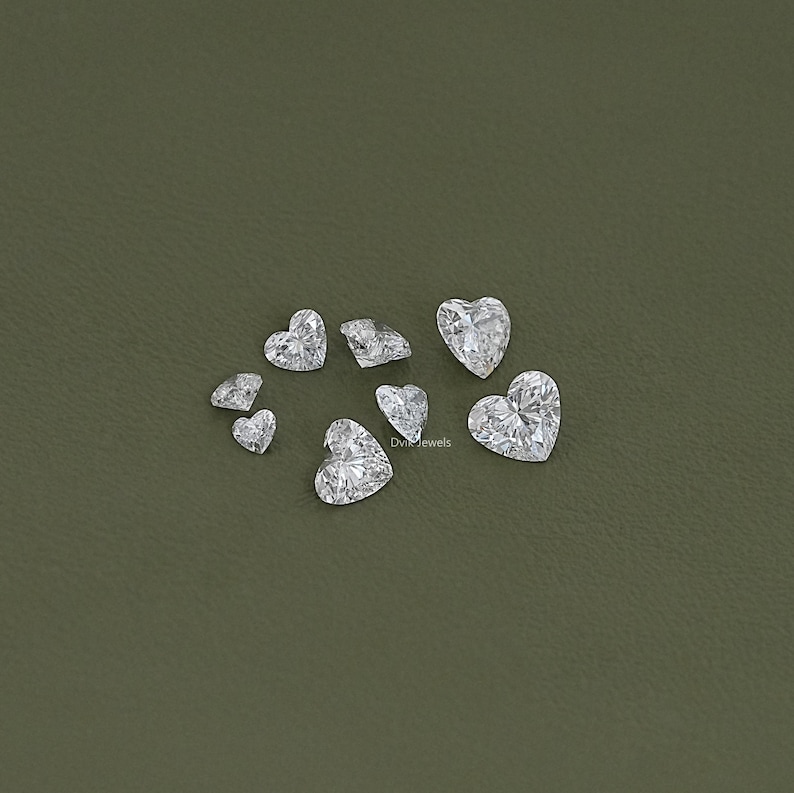 May include: A collection of clear heart-shaped gemstones on a green background.