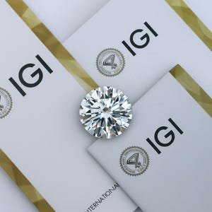 May include: A clear round diamond gemstone with facets, resting on a white surface with the text "IGI International" and a logo with the text "International Gemological Institute" in a circle.