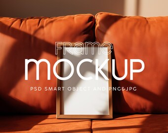 May include: A wooden picture frame with a white interior, labeled "Frame Mockup," rests against orange cushions. The frame is rectangular and has a light brown finish. The text "PSD SMART OBJECT AND PNG&JPG" is below the frame.