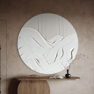 Puede incluir: Una gran obra de arte mural redonda y texturizada, de color blanco, con un diseño abstracto en capas. La obra presenta una combinación de líneas verticales y formas fluidas en forma de olas. Debajo hay una consola de madera.