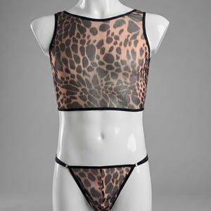 Könnte beinhalten: Ein durchsichtiges Crop-Top und String-Set mit Leopardenmuster. Das Top ist ärmellos mit schwarzem Besatz, und der String hat ein passendes Muster und dünne Träger. Das Set wird auf einer weißen Schaufensterpuppe präsentiert.
