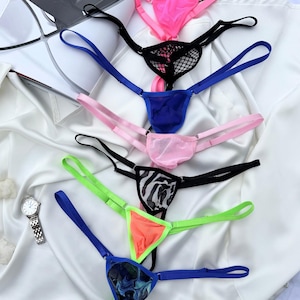 May include: A collection of colorful thong underwear in various designs. The thongs feature vibrant colors like pink, blue, green, and orange, with some showcasing patterns such as zebra print and mesh detailing. A wristwatch is visible in the corner.