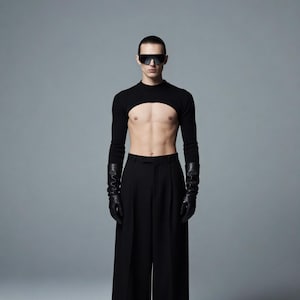 May include: A person wearing a black crop top with long sleeves and a large cutout at the chest, paired with black wide-leg pants and black gloves. The person is also wearing black sunglasses. The background is a solid gray.