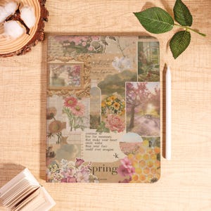 Op de afbeelding: Een decoratief notitieboek met een collage-ontwerp met bloemen- en landschapsafbeeldingen. Een witte stylus ligt naast het notitieboek. Het woord "spring" is zichtbaar. Het notitieboek ligt op een houten oppervlak.