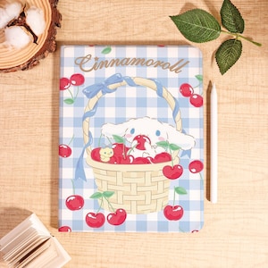 May include: A rectangular tablet case featuring a light blue and white gingham pattern with the text Cinnamoroll at the top. The design shows a white cartoon character sitting in a woven basket filled with red cherries and a small yellow bird.