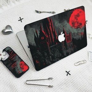 May include: A black laptop skin with a red moon and a dark castle silhouette. The castle has red accents and windows. The skin is designed to fit a laptop.