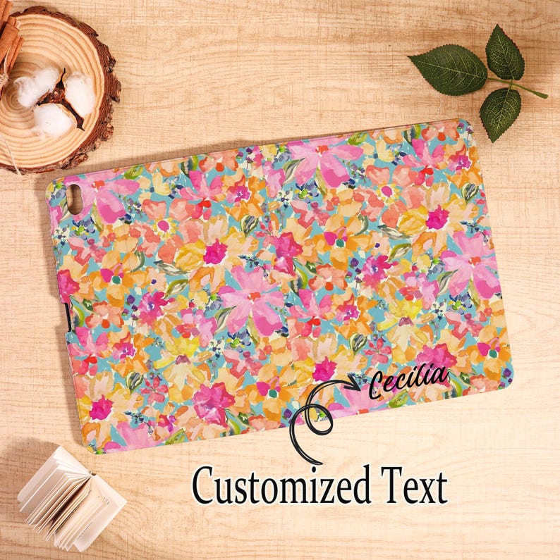 May include: A tablet case with a vibrant floral pattern in pink, yellow, orange, and blue. The case has the name "Cecilia" and the words "Customized Text" printed on it. The case is rectangular.