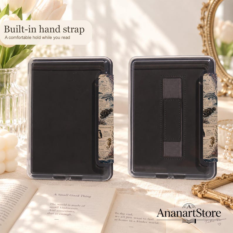 Puede incluir: Dos fundas negras para lector electr&oacute;nico con marcos de pl&aacute;stico transparente y una correa de mano integrada. El lado derecho de cada funda presenta una tira decorativa con ilustraciones marinas vintage y texto. El texto dice Built-in hand strap.