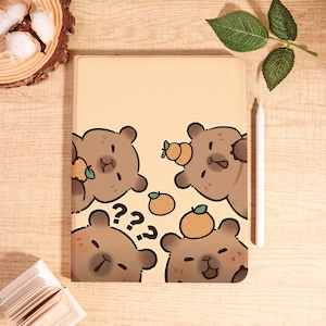 Peut inclure: Étui de tablette beige avec des ours de dessin animé et des oranges. Les ours ont un design mignon avec des points d'interrogation et des accents orange. Un stylet blanc est à côté de l'étui.