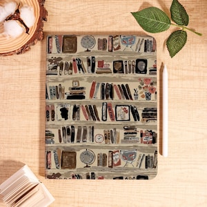 May include: A rectangular notebook with a bookshelf design. The cover features rows of illustrated books, globes, and decorative items in shades of brown, beige, and red. A white stylus rests on the right side. The notebook is on a wooden surface.