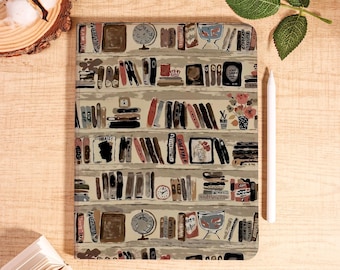 May include: A rectangular notebook with a bookshelf design. The cover features rows of illustrated books, globes, and decorative items in shades of brown, beige, and red. A white stylus rests on the right side. The notebook is on a wooden surface.
