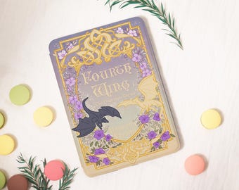 May include: A rectangular case with the text "Fourth Wing" and a decorative design featuring dragons, flowers, and ornate gold accents. The case has a purple background and is surrounded by colorful macarons and greenery.