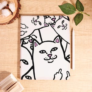 May include: White tablet case featuring a repeating cartoon cat design with black outlines and pink accents. The cat is giving the middle finger. A white stylus rests beside the case on a wooden surface.