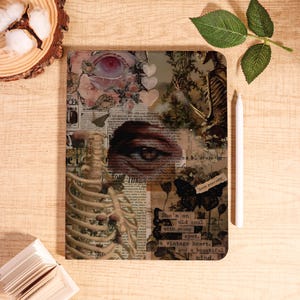 Pode incluir: Uma capa decorativa para tablet com um design de colagem com um esqueleto, um olho e elementos florais. A capa inclui o texto: "She's an old soul with young eyes, a vintage heart, and a beautiful mind." Uma caneta stylus branca está ao lado.