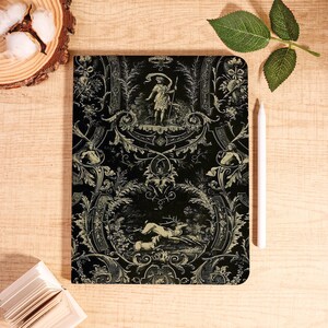 May include: Black and cream-colored notebook with an ornate, vintage design. The cover features a detailed illustration of a classical scene with figures and deer, surrounded by scrolling floral patterns. A white stylus rests beside the notebook.