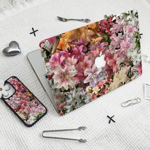 May include: A laptop and phone case with a floral design featuring pink, white, and yellow lilies. The design is a close-up of the flowers, with no background visible.