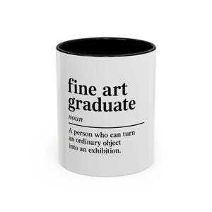 May include: A white ceramic mug with a black interior and rim. The exterior features black printed text that reads: fine art graduate noun A person who can turn an ordinary object into an exhibition. The design is centered on the front of the mug.