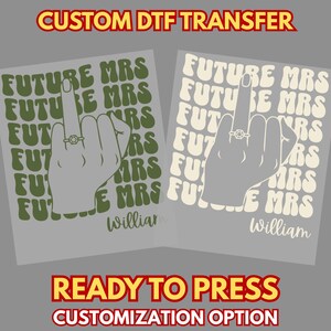 May include: Two custom DTF transfers featuring a hand with a ring making a middle finger gesture, overlaid on repeating text that reads FUTURE MRS. The name William is printed at the bottom. One design is olive green, the other is cream coloured.